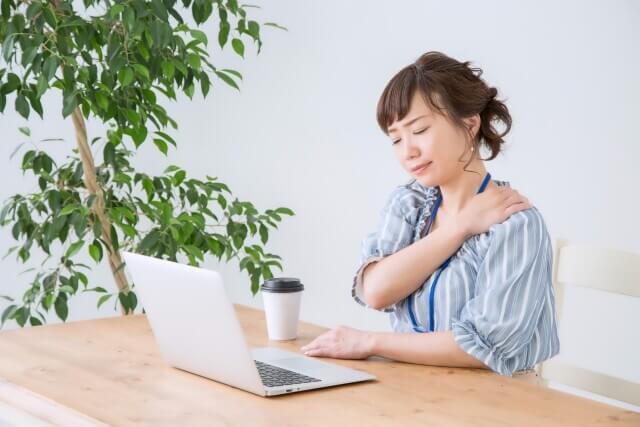 肩こりに悩む女性がパソコン作業中に肩を押さえる様子