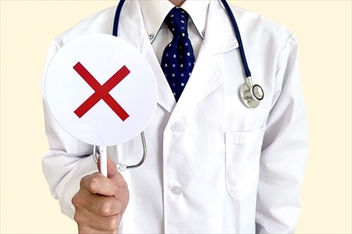 バツ印の札を持つ白衣の医師